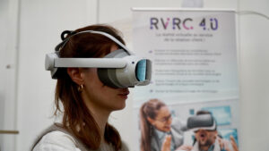 Photographie de profil d'une femme portant un casque de réalité virtuelle blanc dans un cadre professionnel, devant un kakemono promotionnel.