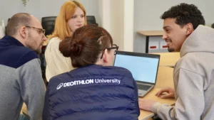 Un groupe de quatre collaborateurs réunis autour d'un ordinateur portable, échangeant des retours dans un cadre professionnel.