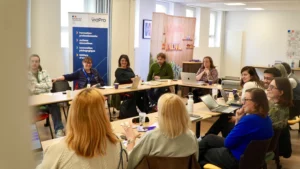 Une assemblée de professionnels installés en arc de cercle autour de tables modulaires lors d'une session de formation ou d'un séminaire.