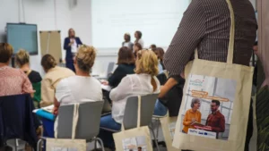 Vue sur un tot bag Résilience et Rebonds, avec en arrière plan l'assemblée qui était présente.