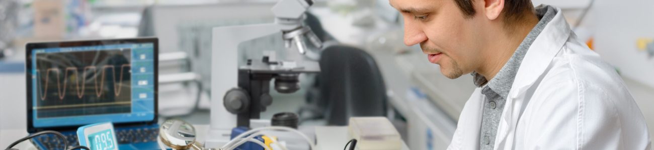 Young energetic male tech or engineer repairs electronic equipment in research facility. Shallow DOF, focus on the face of the worker.