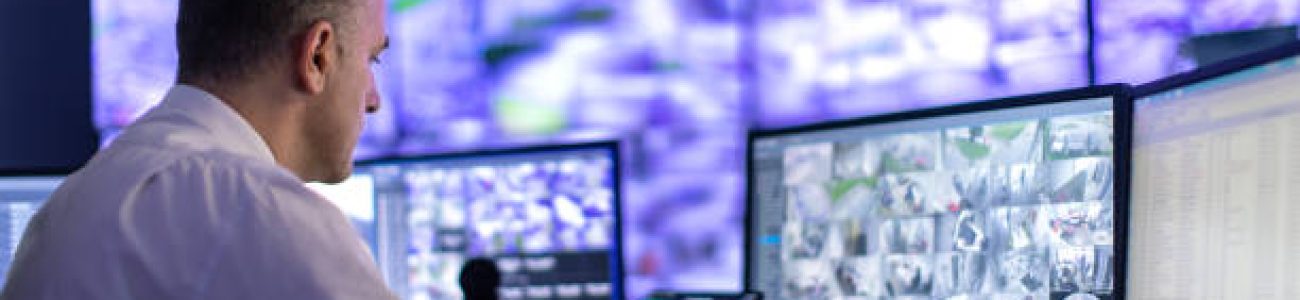 Mature adult man working in surveillance, security and guarding agency and looking at many monitors in front of him.